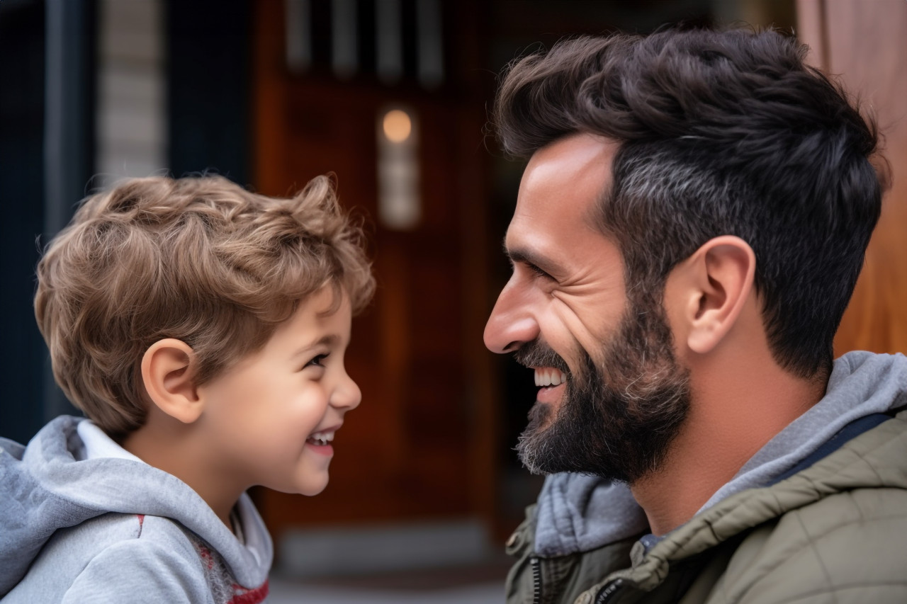 A picture of a handsome dad and his sweet son facing each other and smiling enjoying time at home, indoor activities for kids