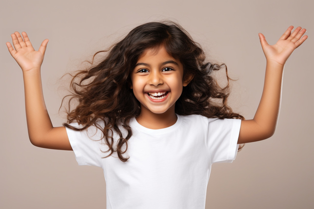 A photo of a happy little indian girl in a white t shirt standing on a beige background with her arms open ready for your advertisement or promotion, kids indoor activities