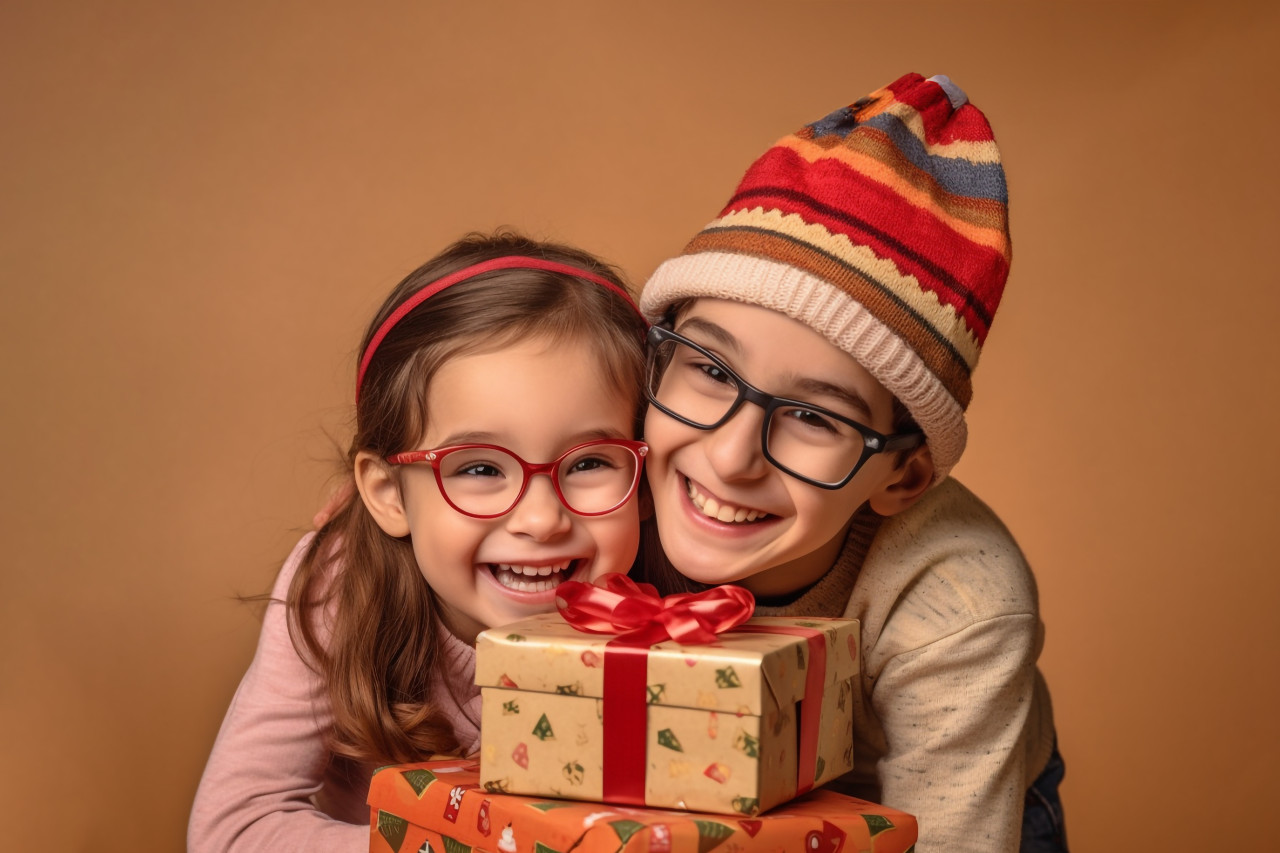A picture of two children hugging and enjoying christmas presents while wearing christmas hats and jumpers on a beige background, christmas festival people image