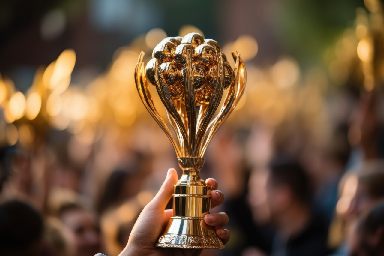 Hand grasps trophy with diverse team cheering in blurred background, employee appreciation day images