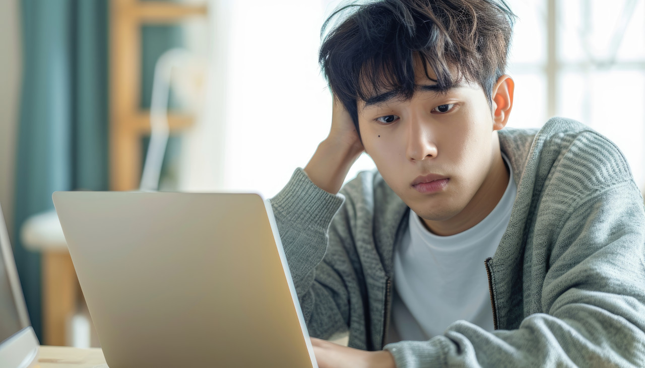 Concerned young asian man hand on head stressfully using laptop at home, financial difficulties photo
