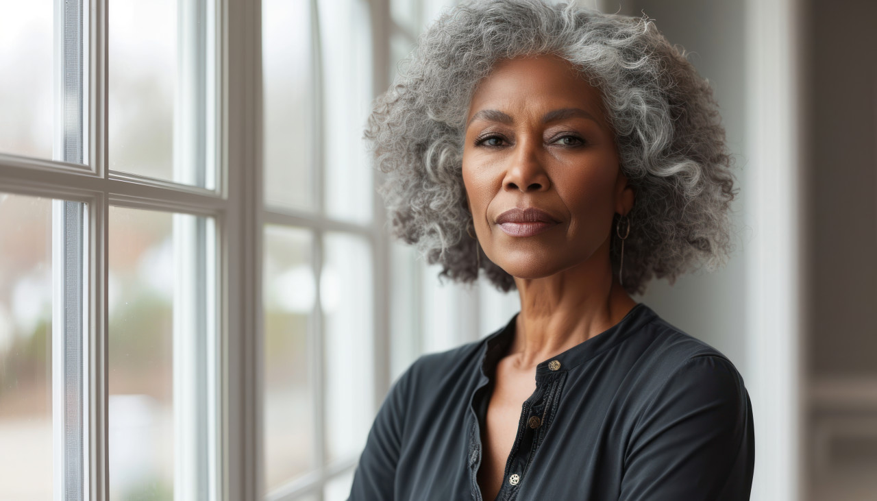 Confident beautiful senior woman of african descent standing near indoor window, grief loss acceptance concept
