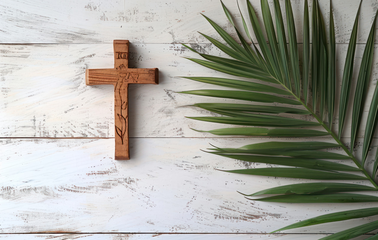 A wooden cross and palm leaf resting on a white table, palm crosses concept
