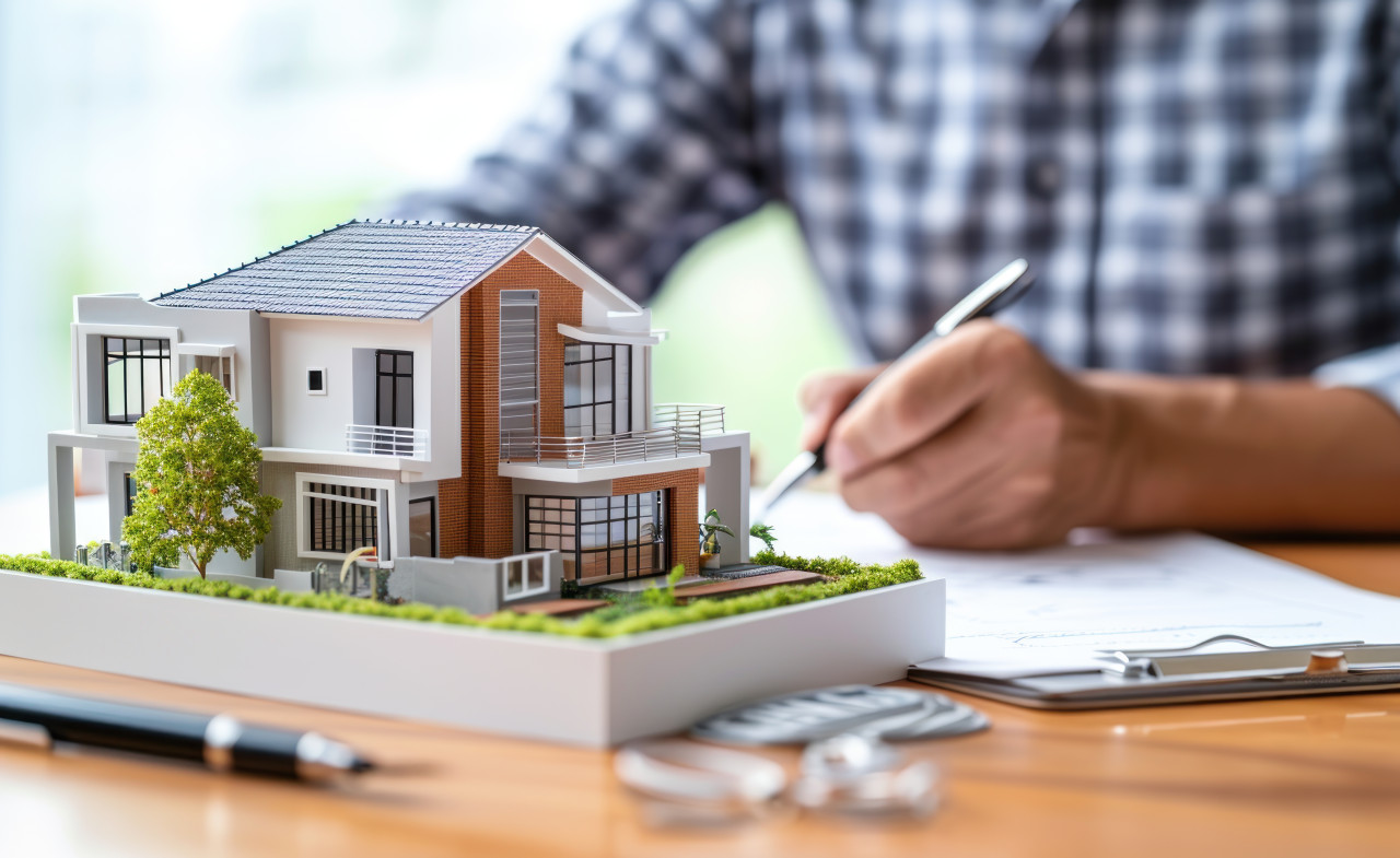 Person holding pen signs over house model, home loan paperwork photo