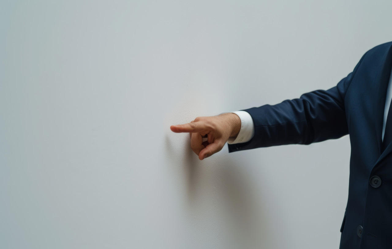 A suited man gestures towards a blank white wall, brand launch photo