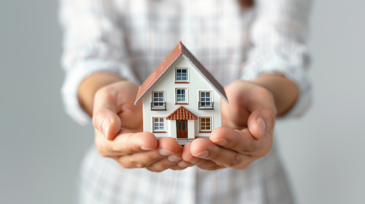 A person holding an icon of their house in miniature form against the background