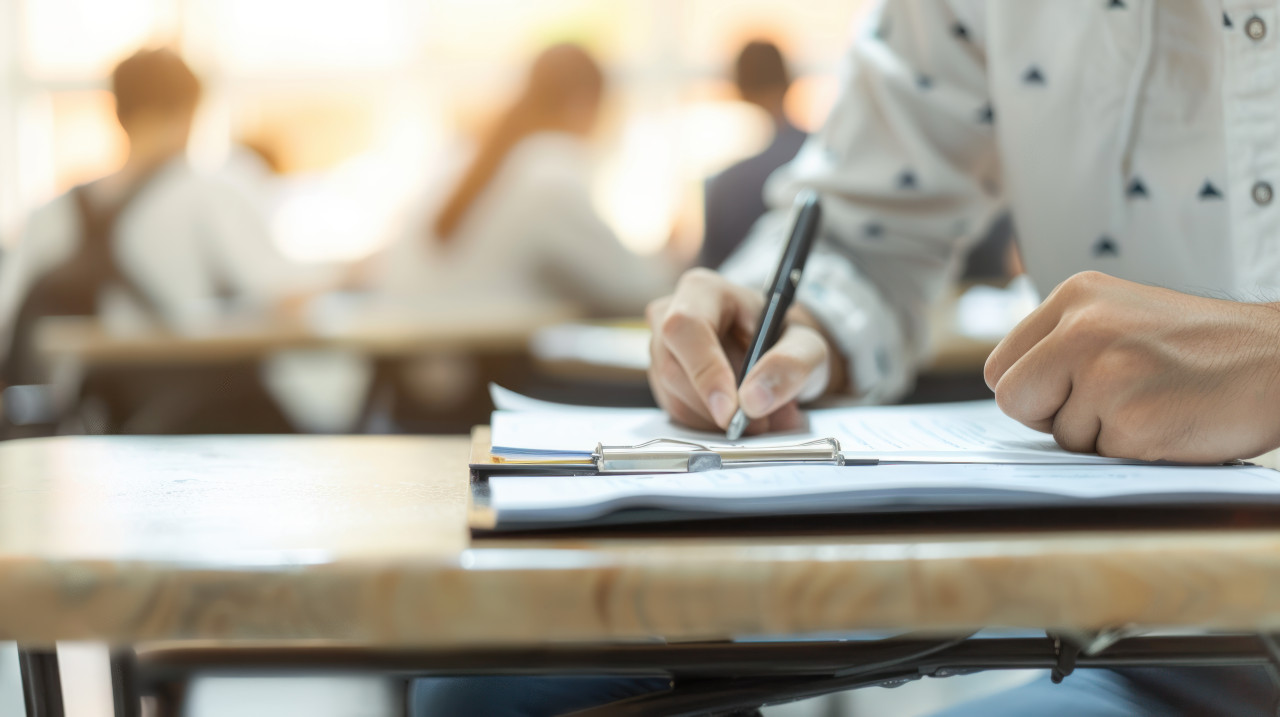 Students concentrated at desk writing exams with pen on paper teachers day celebrations, educational assessment, student taking test