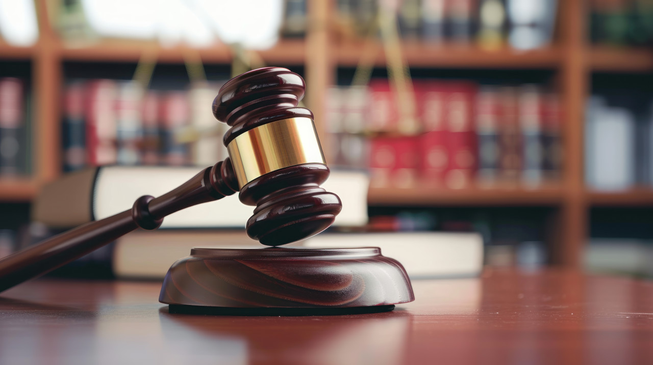 The gavel on a table with a bookcase in the background, indicates legal environment, courtroom tools, judicial equipment