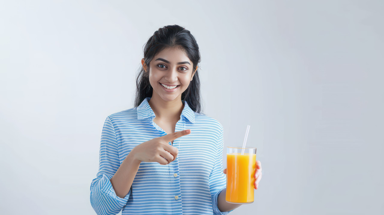 An indian woman pointing at a glass holding orange juice and offering a refreshing beverage, orange juice, hand gesture