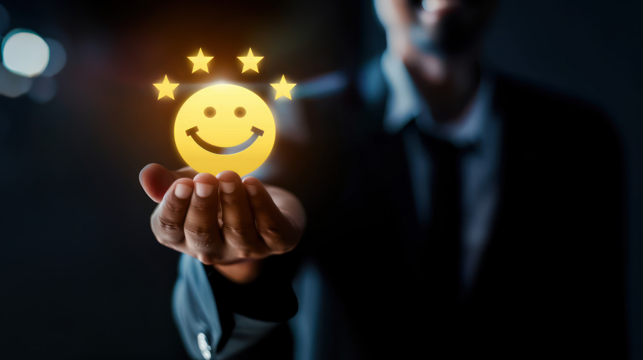 Businessman holding yellow smiley face icon with four stars on dark background representing customer satisfaction, positive feedback, client approval