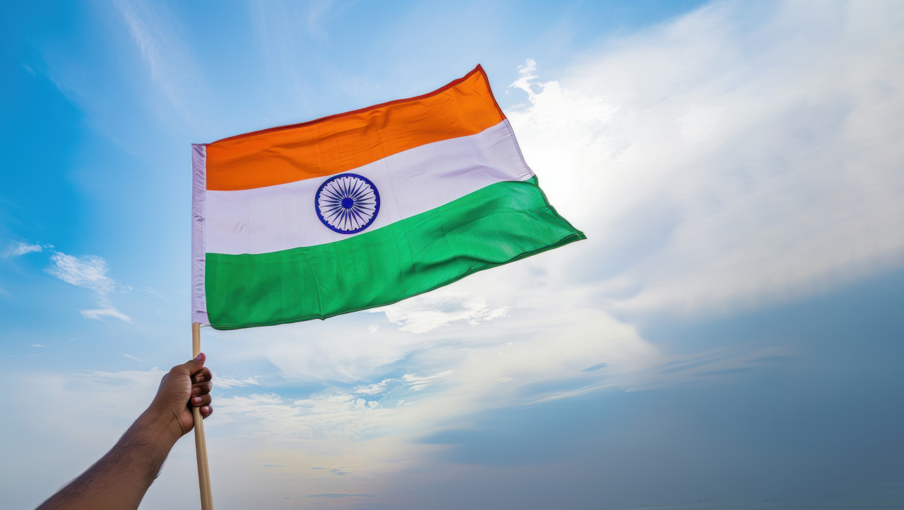 Hand holding an indian flag outdoors against a blue sky background for independence day and republic day, festive outdoor decor, cultural celebration