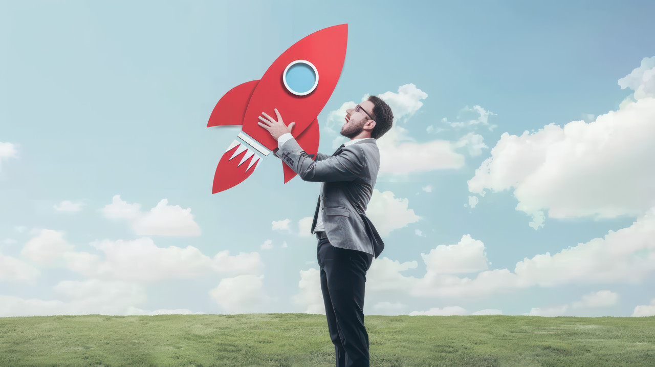 Businessman holding red rocket icon on grass symbolizing startup launch