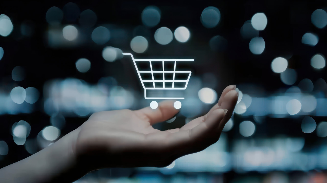 Hand holding shopping cart icon on dark blurred background symbolizing digital online shopping