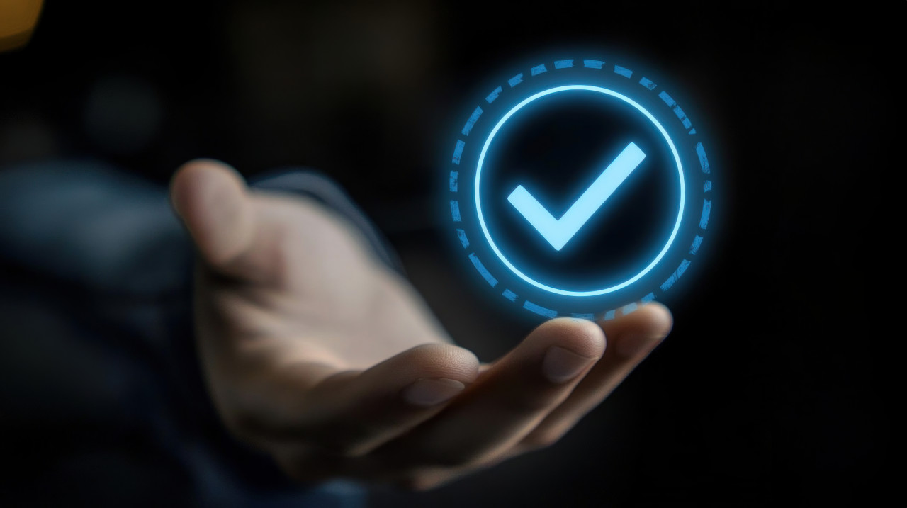 Hand holding glowing blue checkmark icon on dark background showing business performance checklist