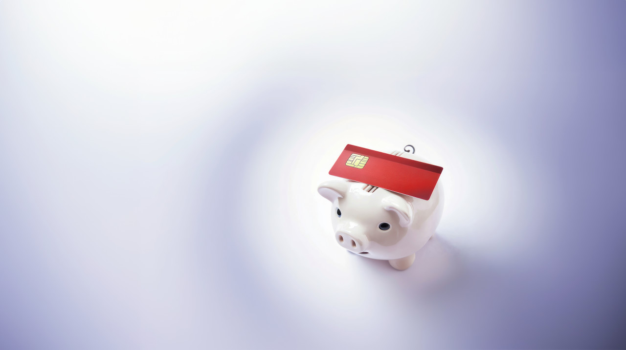 A red credit card is placed on top of a piggy bank atm service concept