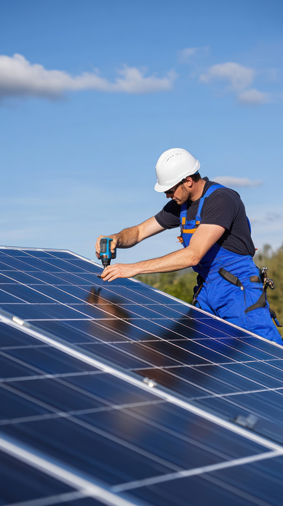 Man in blue overalls and white helmet working on solar panels outdoors on sunny day with clear skies