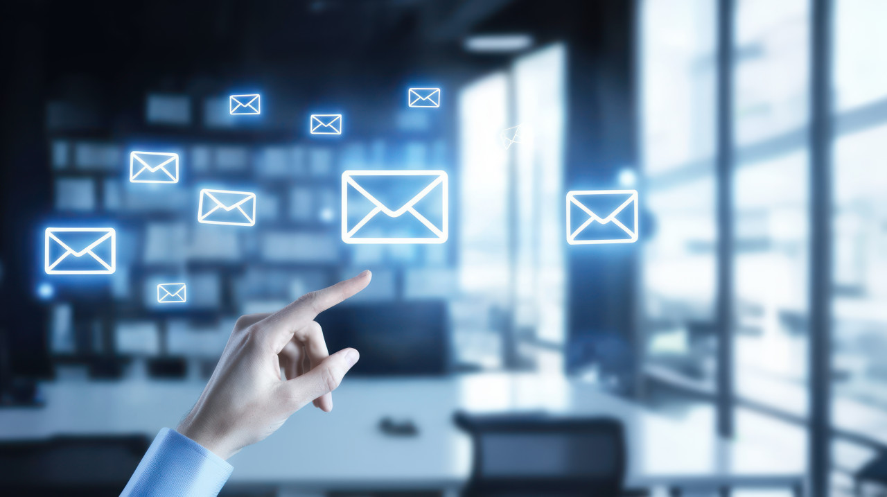 A hand touching an email icon in a blurred office background, demonstrating multichannel marketing and customer conversion strategies
