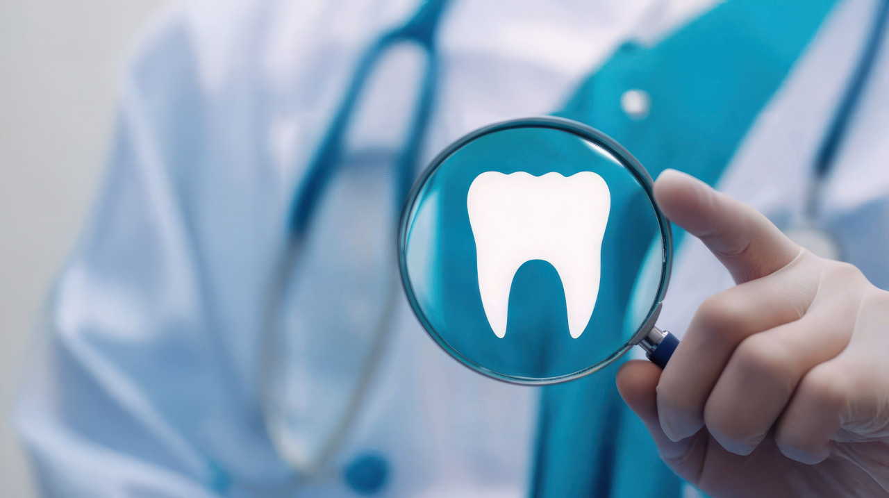 Dental doctor holds a magnifying glass with a tooth symbol on it against a professional medical background, represents detailed dental care for tooth extraction, jaw surgery, and dental implants