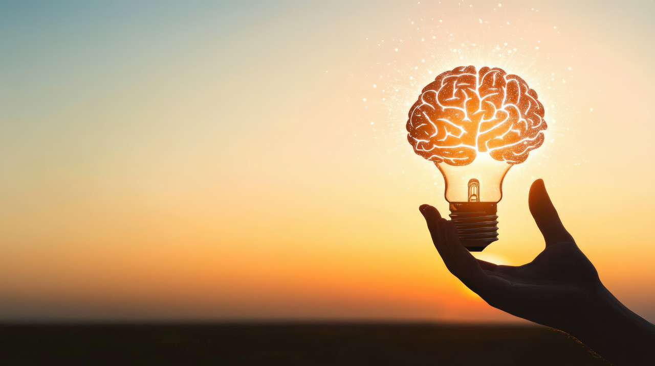 A hand holds an illuminated light bulb with a glowing brain inside against a gradient background, symbolizing neurology, ocd, schizophrenia, and pediatric neurologist insights