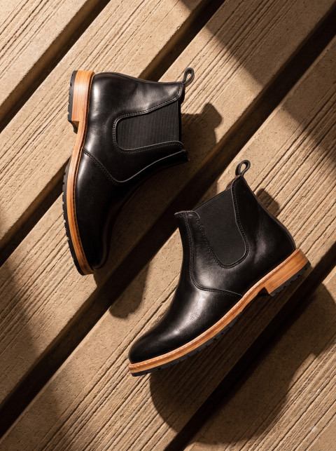 Black Chelsea Boots Flat Lay on Grooved Wood Deck